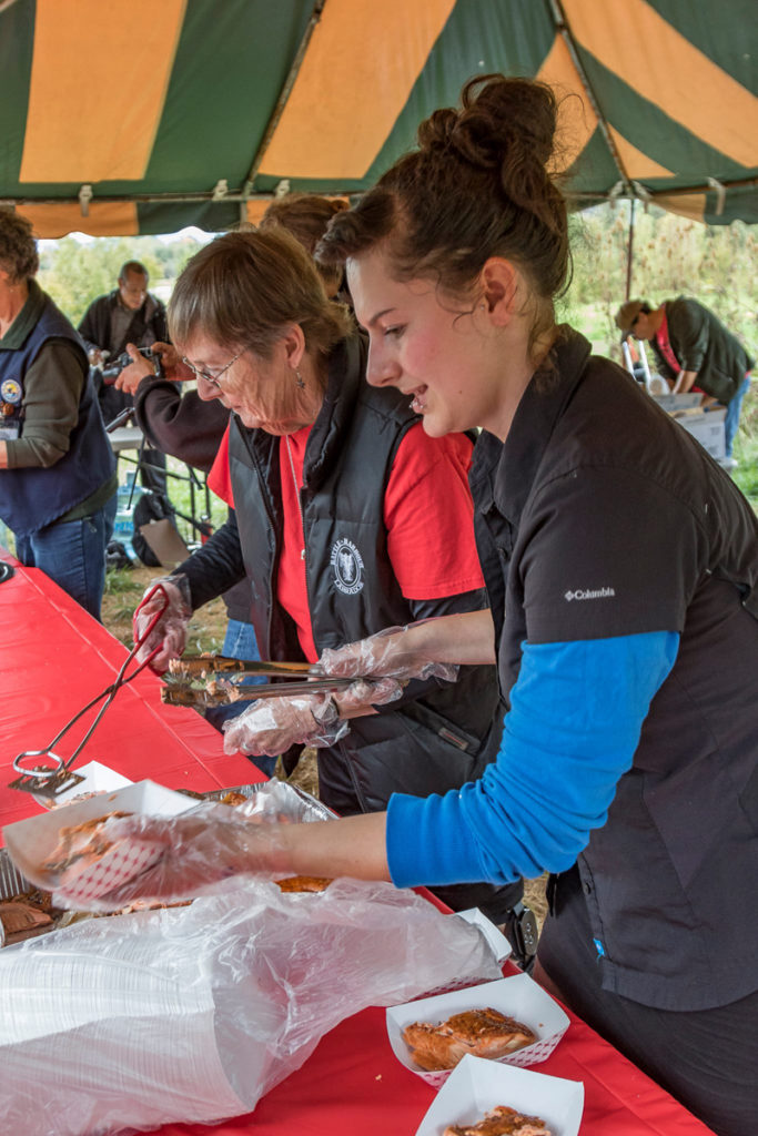 Kaye Duncan, Plankhouse volunteer and Sarah Hill, Plankhouse director, serversalmon at the traditional salmon bake at the Cathlapotle Plankhouse, Sun., Oct. 2 at the Carty Unit of the Ridgefield National Wildlife Refuge during Bird Fest. Photo by Mike Schultz.