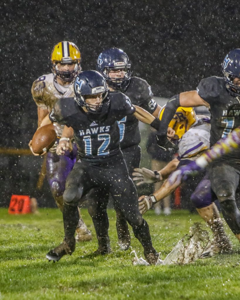 Hockinson quarterback Canon Racanelli (12) runs through the mud for a big gain against Columbia River Friday. Photo by Mike Schultz.