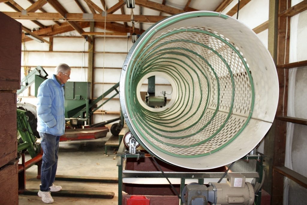 Instead of buying an expensive piece of processing equipment, Ray Young (left) and Carolyn Young (not pictured), owners of Allen Creek chestnut farm in Ridgefield, made this ingenious chestnut sorter to separate the nuts into batches of small, which are milled into chestnut flour, medium, large and extra-large. The hoses keep the chestnuts moving through the spiraling sorter and the holes sort them into their size-specific bins below. Photo by Kelly Moyer