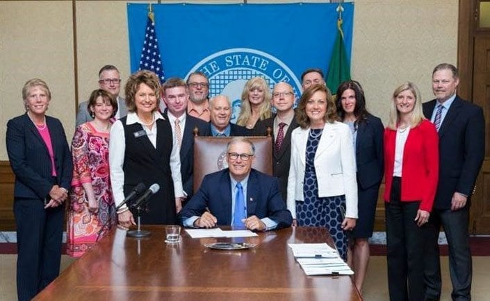 Gov. Jay Inslee (seated) signed a slimmed-down companion version of Rep. Liz Pike’s short-line railroad jobs bill last week. Pike is shown here standing on the left of Inslee. To the right of Inslee is Sen. Lynda Wilson, who sponsored the Senate’s companion version of Pike’s bill. Also pictured is Rep. Vicki Kraft (second from right) and Clark County Councilor Julie Olson (far left). Photo courtesy of Washington State House Republican Communications