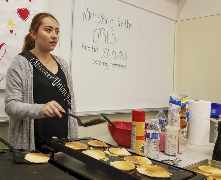 Kaitlyn Milliken proudly displays her (Miss)ter Union sash as she makes more pancakes Thursday morning at Union High School. Milliken asked for donations “for the babies” as the (Miss)ter Union Pageant raises funds for the neonatal intensive care unit at PeaceHealth Southwest Medical Center. Photo by Paul Valencia