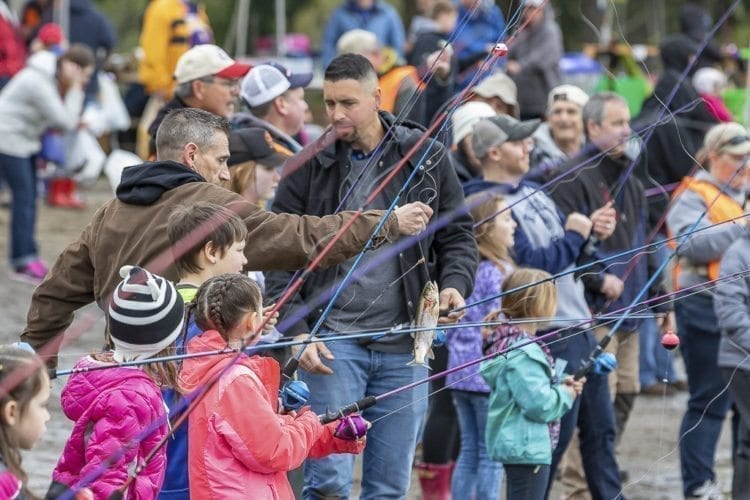 A man helps a young angler bring in a fish during the Klineline Kids Fishing Derby at Salmon Creek Park in Vancouver Saturday. Photo by Mike Schultz