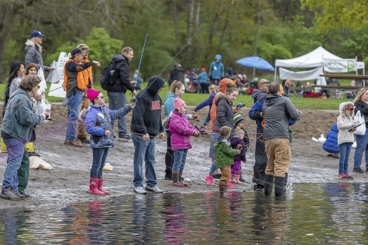 Children, adults and volunteers stand along the beach at Klineline Pond in Salmon Creek Park Saturday morning for the Klineline Kids Fishing Derby. Photo by Mike Schultz