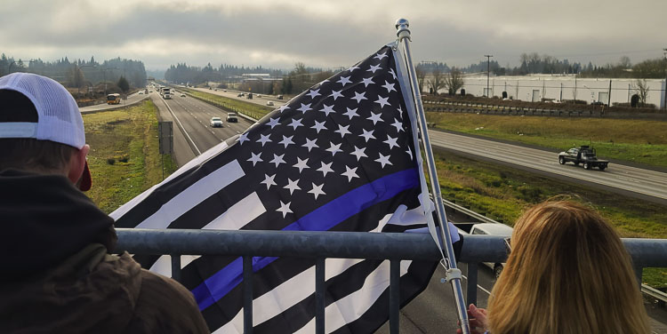 Flags were seen throughout Clark County on Tuesday, including at the Ridgefield exit overpass on Interstate 5 as community members got in position to pay their respects for the procession for Vancouver police officer Donald Sahota. Photo by Paul Valencia