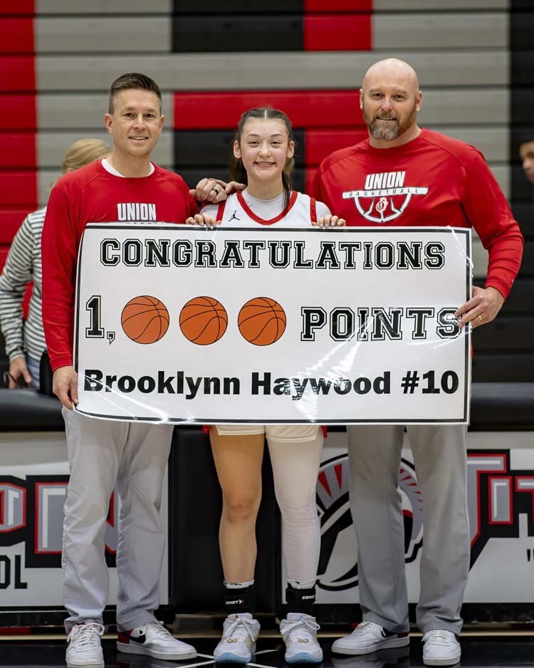 Union sophomore Brooklynn Haywood holds up a banner along with head coach Gary Mills (left) and assistant coach Todd Spike after Monday’s game. Haywood now has 1,011 career points in 40 games. Photo courtesy Heather Tianen