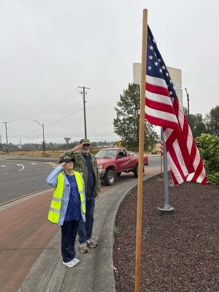 Judith Wyatt and Doug Gregg salute one of the flags they posted Thursday morning along a roundabout in Ridgefield. Photo courtesy Jen McDonnell