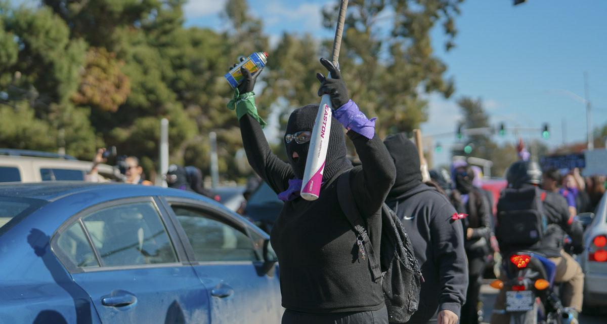 A masked protester raises a bat and spray paint can during a demonstration. Photo courtesy Barbara Zandoval/Unsplash