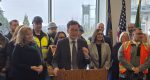 Washington Governor Bob Ferguson, with the mayor of Vancouver Anne McEnerny-Ogle on his right and the Interstate Bridge in the background, outlines his vision for the immediate future of the replacement bridge project. Photo by Paul Valencia